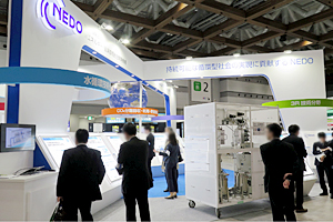Photo of NEDO booth with many visitors observing items on display such as a methanation system