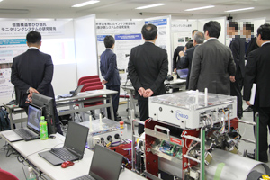 Photo of symposium attendees observing actual monitoring system and panel displays at exhibit