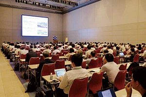 Photo of large audience listening to presentations by representatives of companies entrusted to carry out projects