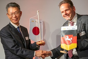 Executive Director YUMITORI and Dr. Keussen, CTO at EWE AG are shaking hands when exchanging the national flag of Japan and the state flag of Lower Saxony of Germany