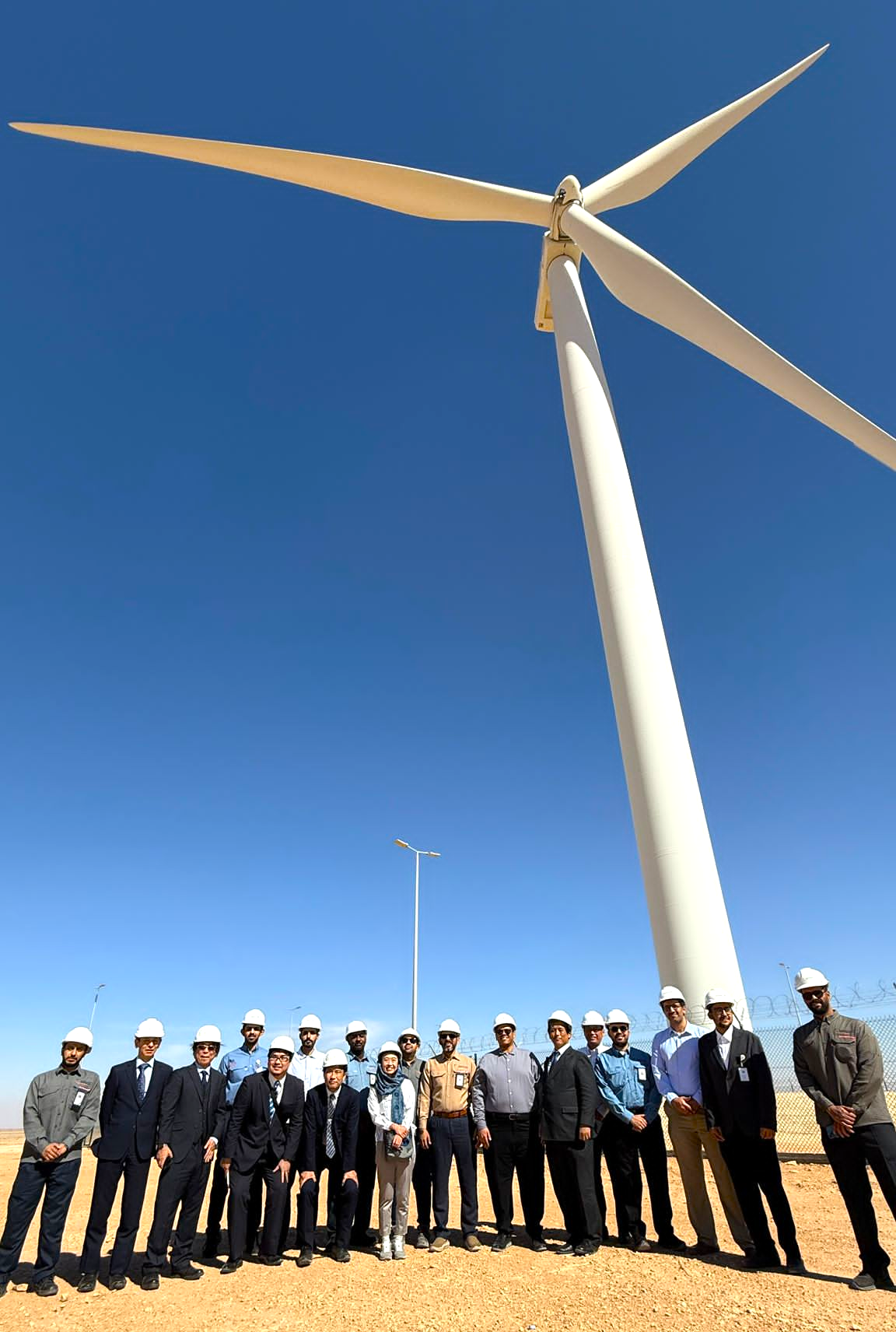 Group photo at the project site in Huraymila, beneath the wind turbine