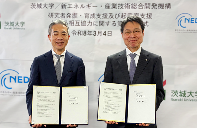 署名した覚書を掲げて微笑む茨城大学太田学長とNEDO吉田理事の写真